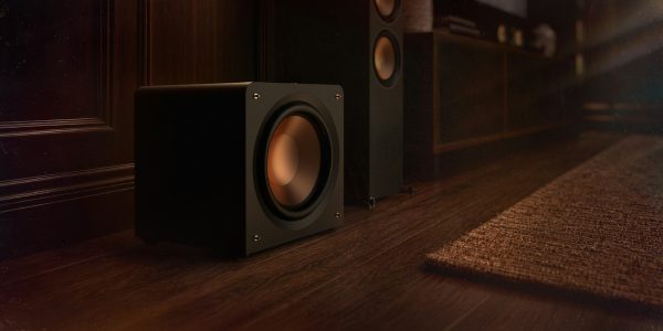 Klipsch Reference Premiere Compact Subwoofer beside a media console and floorstanding speakers