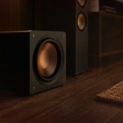 Klipsch Reference Premiere Compact Subwoofer beside a media console and floorstanding speakers